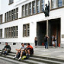 A photograph of students sitting and standing outside of the entrance to the Neue Universität.