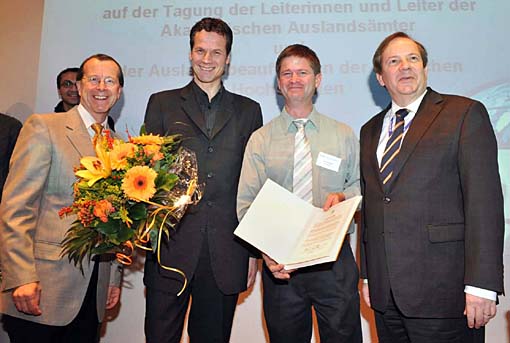 Joachim Bürkert (mit Blumenstrauß) und Dr. Keith Hall (mit Urkunde) freuen sich über die Auszeichnung. Links: Ministerialdirektor Martin Kobler vom Auswärtigen Amt; rechts: Professor Stefan Hormuth, Präsident des DAAD.  